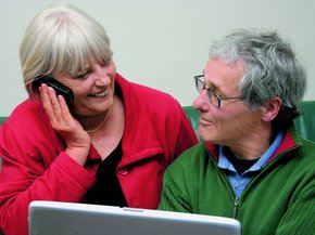 Stariji par ispred laptopa gleda jedno u drugo dok žena razgovara na telefon